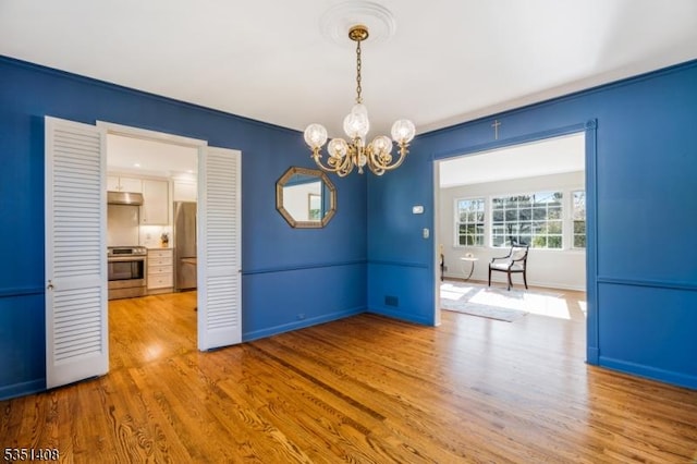 unfurnished dining area featuring crown molding, baseboards, light wood-type flooring, and a notable chandelier