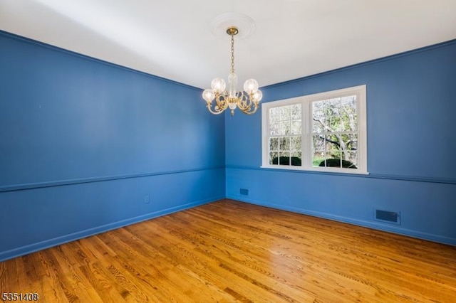 empty room with baseboards, wood finished floors, and a notable chandelier