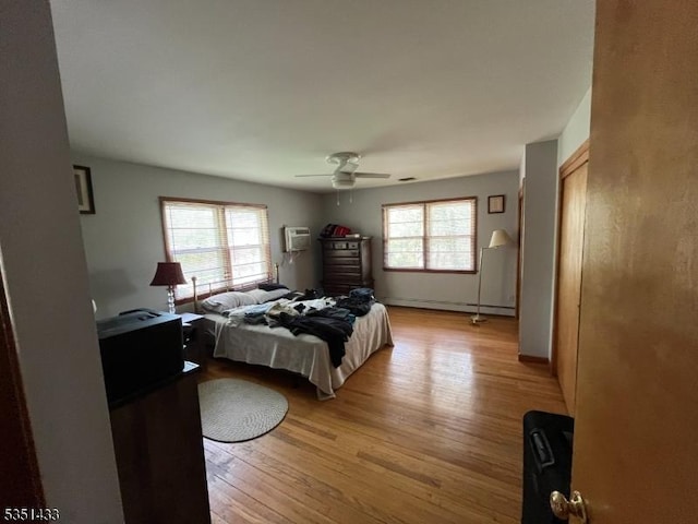 bedroom featuring ceiling fan, a wall mounted AC, a baseboard heating unit, and light wood finished floors