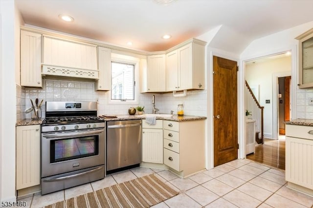kitchen featuring light tile patterned flooring, light stone counters, a sink, appliances with stainless steel finishes, and backsplash