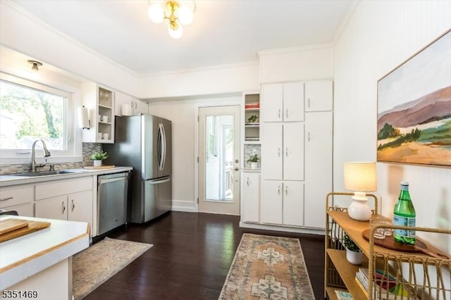 kitchen with appliances with stainless steel finishes, a sink, light countertops, ornamental molding, and dark wood-type flooring