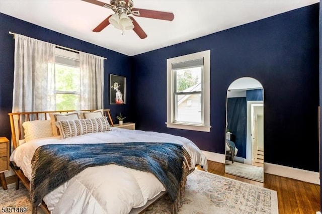 bedroom with arched walkways, multiple windows, baseboards, and wood finished floors