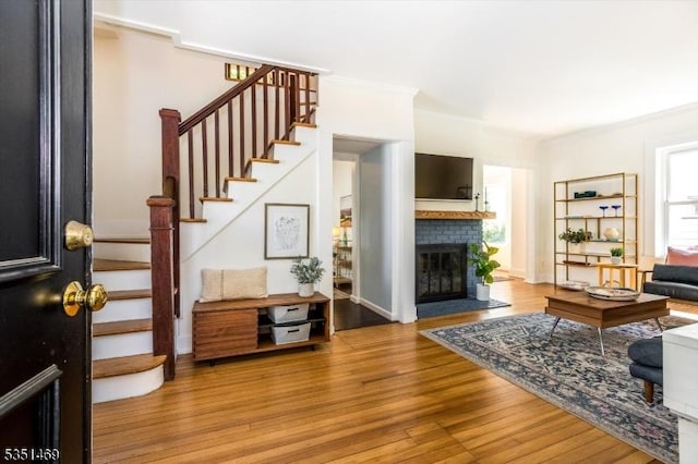 living area with light wood-style floors, crown molding, a brick fireplace, and stairs