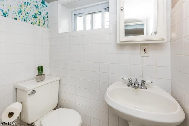 half bath featuring a sink, tile walls, and toilet