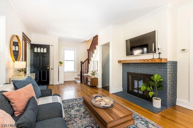 living area featuring a fireplace, stairs, baseboards, wood finished floors, and ornamental molding