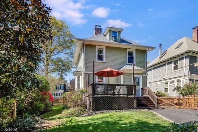 back of property with a wooden deck, fence, a yard, and a chimney