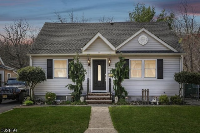 bungalow with entry steps, a lawn, and roof with shingles
