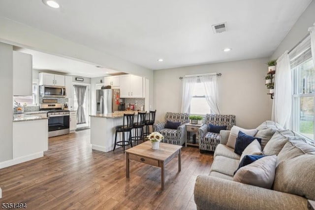 living area featuring recessed lighting, visible vents, a wealth of natural light, and dark wood-type flooring