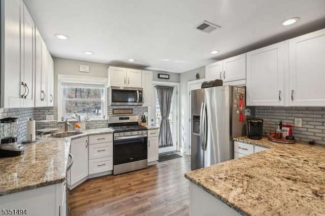 kitchen with light stone counters, a sink, appliances with stainless steel finishes, white cabinetry, and visible vents