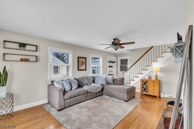 living room featuring baseboards, a ceiling fan, wood finished floors, and stairway