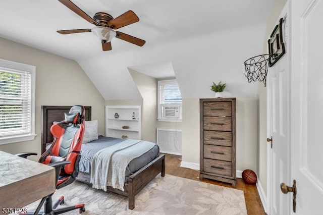 bedroom with radiator heating unit, vaulted ceiling, wood finished floors, and multiple windows