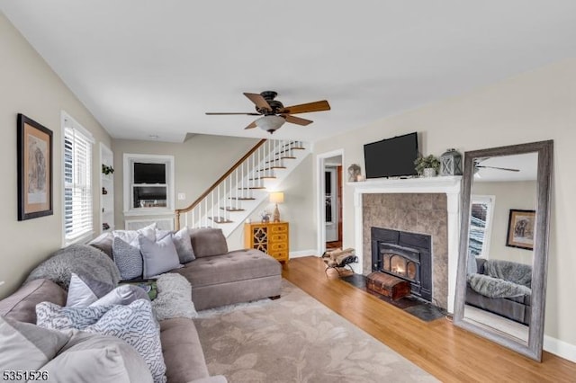 living room featuring light wood finished floors, a wealth of natural light, a ceiling fan, and stairs
