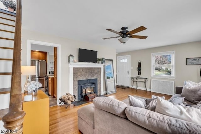 living area featuring radiator heating unit, ceiling fan, a tiled fireplace, and light wood-type flooring