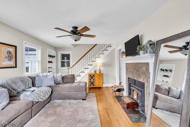 living room featuring wood finished floors, a tile fireplace, a ceiling fan, and stairway