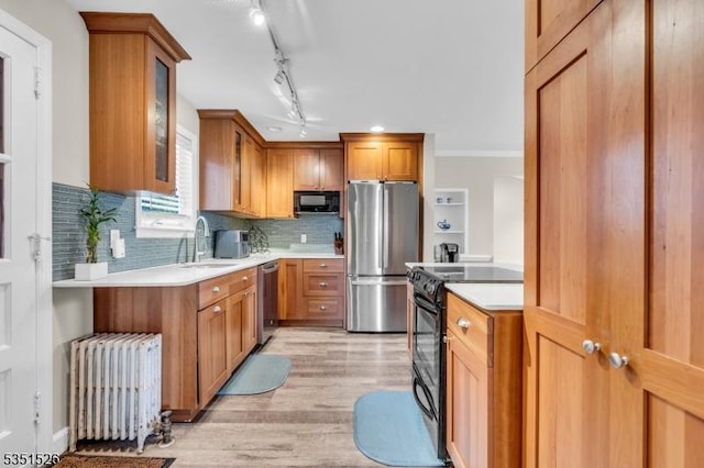 kitchen with radiator heating unit, a sink, black appliances, light wood-type flooring, and light countertops