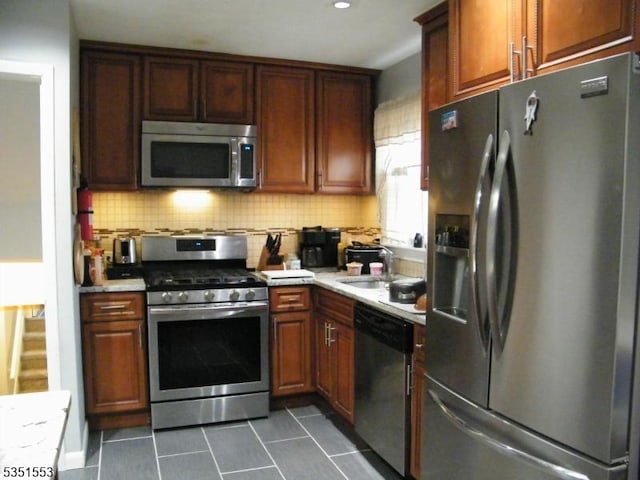 kitchen featuring a sink, light countertops, stainless steel appliances, decorative backsplash, and dark tile patterned floors