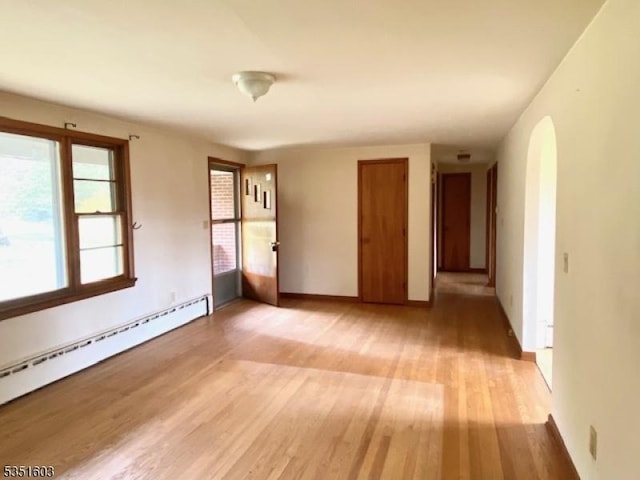 unfurnished room with baseboards, light wood-style flooring, and a baseboard radiator