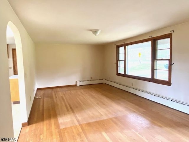 spare room featuring arched walkways, baseboards, and light wood-style flooring