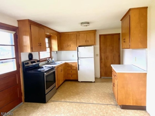 kitchen featuring freestanding refrigerator, light countertops, brown cabinetry, and stainless steel range with electric stovetop