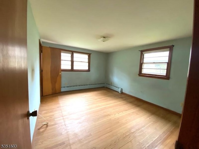 spare room featuring baseboards, a baseboard radiator, light wood-style flooring, and a healthy amount of sunlight