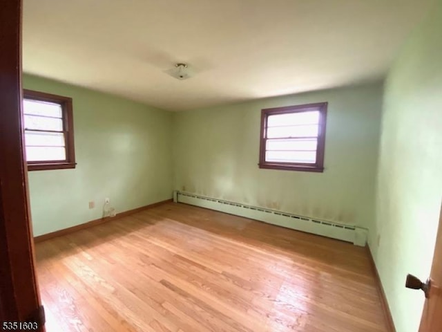 spare room with baseboards, baseboard heating, and light wood-type flooring