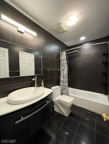 bathroom featuring vanity, shower / bath combo with shower curtain, toilet, tile walls, and tile patterned floors