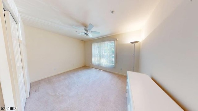 unfurnished room with light colored carpet, a ceiling fan, and baseboards
