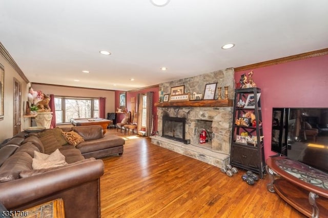 living area featuring a stone fireplace, wood finished floors, crown molding, and recessed lighting