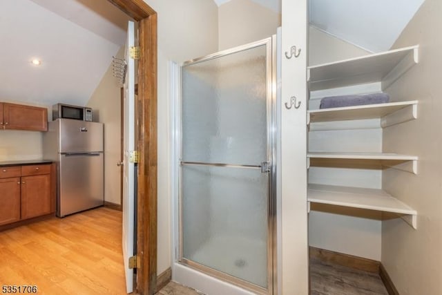 full bath with wood finished floors, a shower stall, vaulted ceiling, and baseboards