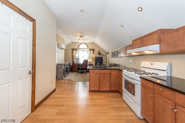 kitchen with gas range gas stove, light wood-style flooring, under cabinet range hood, a wall mounted air conditioner, and dark countertops
