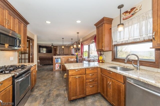kitchen with a sink, stainless steel appliances, light stone countertops, a peninsula, and brown cabinetry