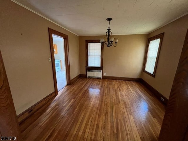 unfurnished dining area with wood-type flooring, a chandelier, a healthy amount of sunlight, and radiator heating unit