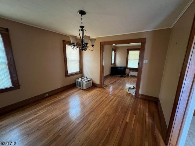 unfurnished dining area featuring wood-type flooring, baseboards, crown molding, and a chandelier