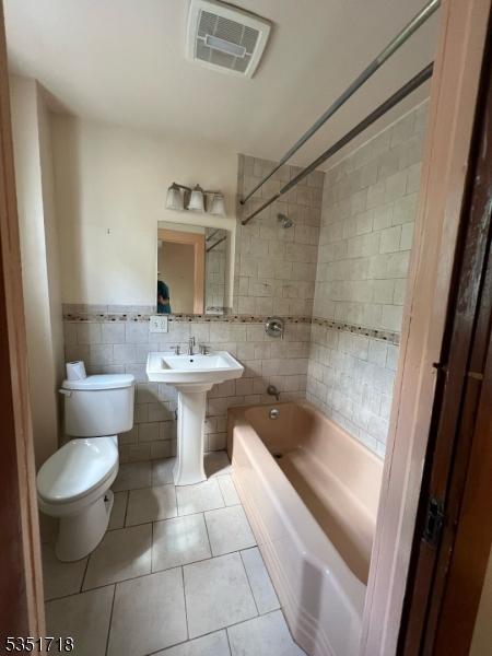 full bath with bathtub / shower combination, toilet, tile patterned floors, tile walls, and visible vents