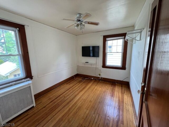 empty room with wood-type flooring, a ceiling fan, plenty of natural light, and radiator
