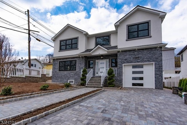 view of front of house featuring stone siding, fence, an attached garage, stucco siding, and decorative driveway