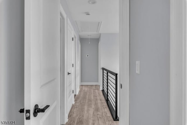 hall with light wood-type flooring, attic access, and baseboards