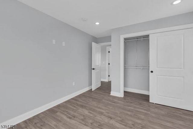 unfurnished bedroom with recessed lighting, wood finished floors, a closet, and baseboards