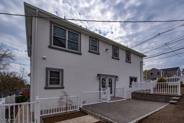 rear view of property featuring stucco siding, fence, a patio area, and french doors
