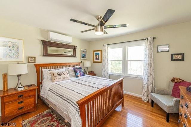bedroom with a wall mounted AC, wood finished floors, baseboards, and ceiling fan