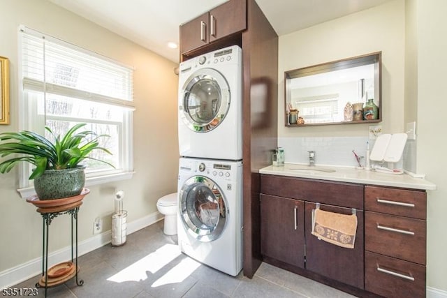 clothes washing area with laundry area, light tile patterned floors, a sink, stacked washing maching and dryer, and baseboards