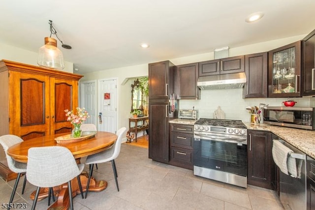 kitchen with decorative backsplash, glass insert cabinets, light stone counters, under cabinet range hood, and appliances with stainless steel finishes