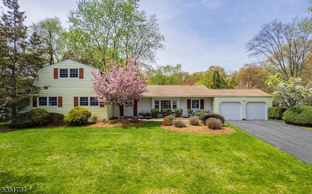 traditional home featuring an attached garage, a front yard, and aphalt driveway