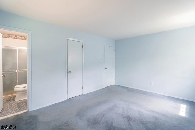 unfurnished bedroom with baseboards, ensuite bathroom, and carpet