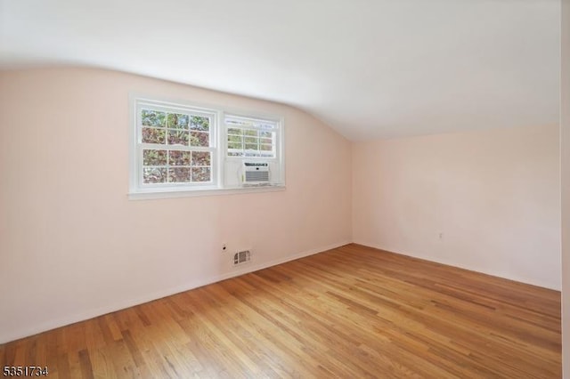 additional living space with visible vents, light wood-style flooring, cooling unit, and vaulted ceiling