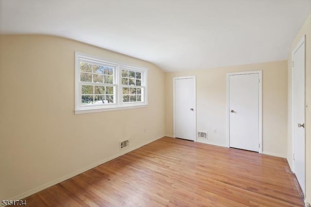 unfurnished bedroom with visible vents, baseboards, light wood-style floors, and lofted ceiling