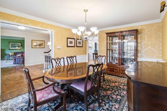 dining space with ornamental molding, wainscoting, a decorative wall, wallpapered walls, and a chandelier