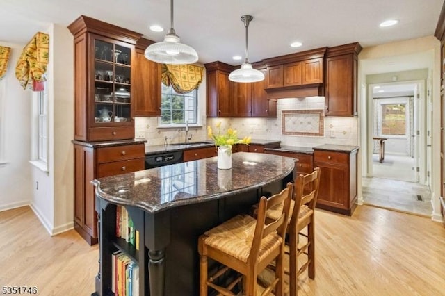 kitchen featuring decorative backsplash, a kitchen breakfast bar, light wood-type flooring, a sink, and dark stone counters