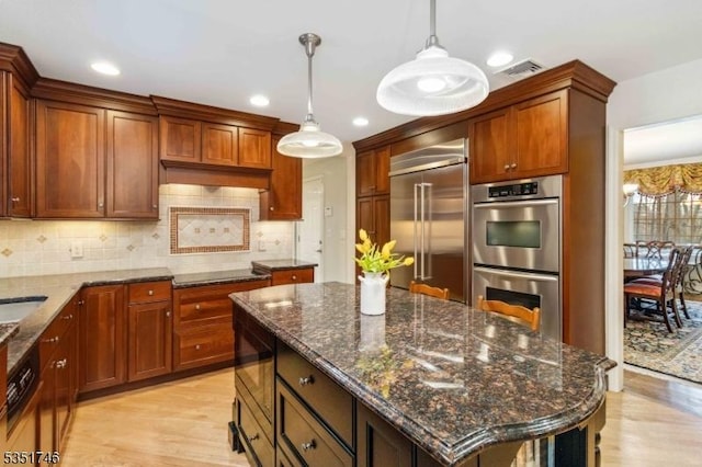 kitchen with built in appliances, a kitchen island, light wood finished floors, and visible vents