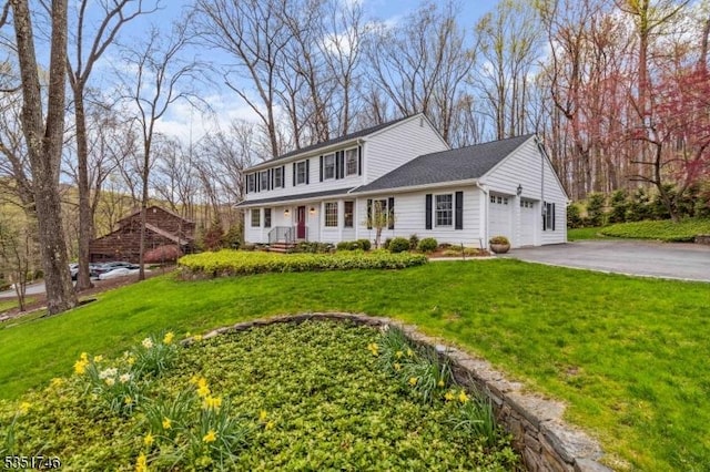 traditional home featuring an attached garage, a front lawn, and aphalt driveway